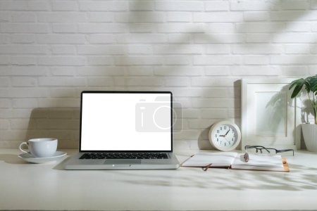 Photo for Front view of laptop with empty display, picture frame, coffee cup and notebook on white table. - Royalty Free Image