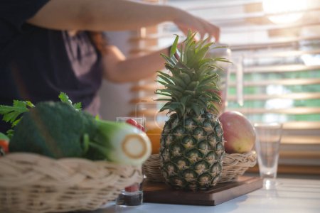 Photo for Fresh tropical fruit and vegetable on table with woman making healthy smoothie in background. Healthy lifestyle. - Royalty Free Image