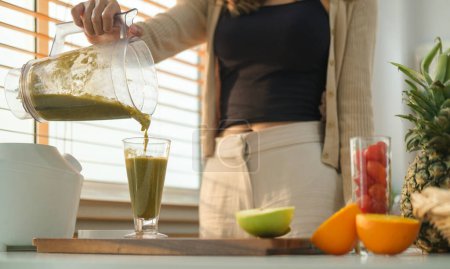 Photo for Healthy young woman pouring reen vegetable smoothie into a glass. Healthy eating, health, nutrition and vegetarian. - Royalty Free Image