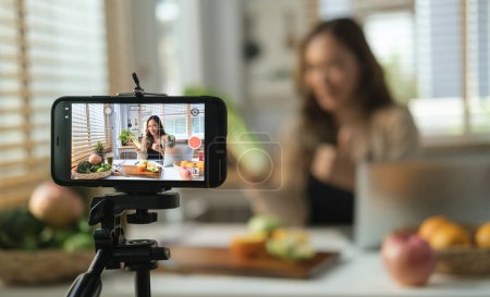 Photo for Beautiful young female health coach recording on a smart phone her vlog about healthy eating. - Royalty Free Image