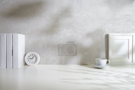 Photo for Comfortable workplace with blank picture frame, books, clock and coffee cup on white table. Copy space for your text. - Royalty Free Image