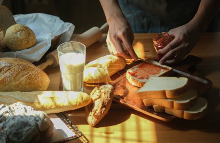 Téléchargez les photos : Homme utilisant couteau propagation maison confiture de fraises sur une tranche de pain, préparer le petit déjeuner dans la cuisine. - en image libre de droit