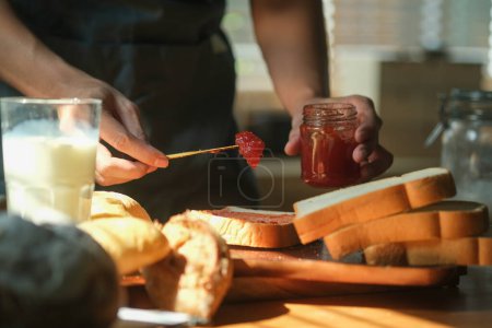 Téléchargez les photos : Homme propagation de confiture de framboise douce sur le pain grillé et prendre le petit déjeuner à la maison. - en image libre de droit
