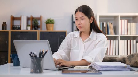 Foto de Atractiva joven empresaria sentada en el escritorio en la oficina en casa y trabajando en el ordenador portátil. - Imagen libre de derechos