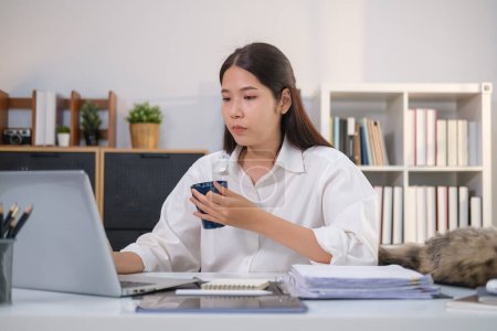 Téléchargez les photos : Millennial asiatique femme boire du café et vérifier les e-mails d'affaires sur ordinateur portable. - en image libre de droit