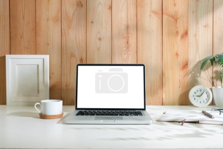Foto de Vista frontal de la computadora portátil con pantalla en blanco, marco de imagen, taza de café y planta en maceta en el escritorio blanco. - Imagen libre de derechos