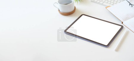 Foto de Tableta digital con pantalla vacía en taza de café y bloc de notas en escritorio de oficina blanco. Copia espacio para tu texto. - Imagen libre de derechos