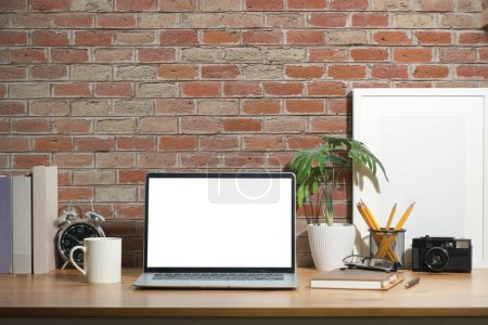 Foto de Elegante lugar de trabajo con computadora portátil, papelería, planta de interior y marco de imagen en la mesa de madera. - Imagen libre de derechos