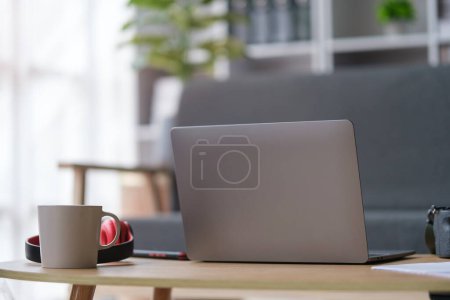 Téléchargez les photos : Derrière un ordinateur portable, une tasse de café et un casque sur une table en bois dans le salon. - en image libre de droit