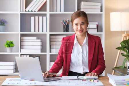 Foto de Retrato de una exitosa mujer de negocios en traje rojo de lujo usando computadora portátil y trabajando con documento en la oficina. - Imagen libre de derechos