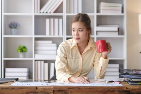 Téléchargez les photos : Jeune femme d'affaires buvant du café et analysant les résultats du travail, faisant de la paperasse sur le lieu de travail. - en image libre de droit