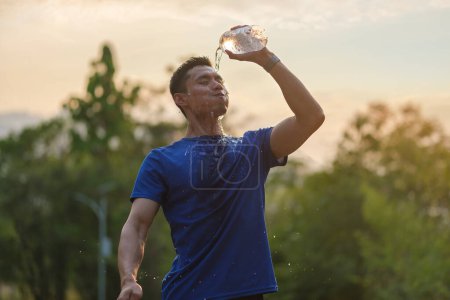 Photo for Tired athletic man cooling himself after training by squirting water into his face from a bottle. - Royalty Free Image