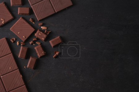 Téléchargez les photos : Vue du dessus des morceaux de chocolat noir sur fond noir avec espace de copie. - en image libre de droit
