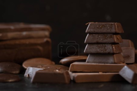 Photo for Stack of chocolate cubes and dark chocolate bars on black background. Dessert food background. - Royalty Free Image