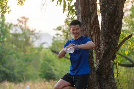 Foto de Sportsman checking his smartwatch while running in city park. Sport, exercise and fitness outdoors in nature. - Imagen libre de derechos