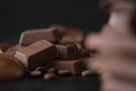 Téléchargez les photos : Gros plan de cubes de chocolat et de pépites de chocolat sur fond noir. Dessert alimentaire fond. - en image libre de droit