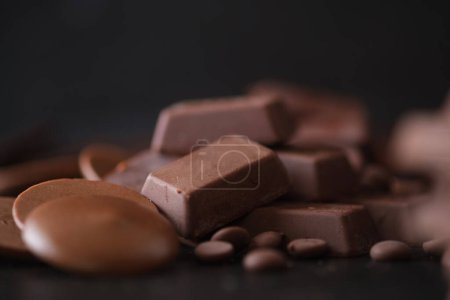 Téléchargez les photos : Bouton chocolat, cubes de chocolat et pépites de chocolat sur fond sombre. - en image libre de droit