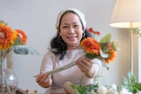 Foto de Mujer madura positiva disfrutando de la organización de flores, haciendo hermoso ramo de flores en la acogedora sala de estar. - Imagen libre de derechos