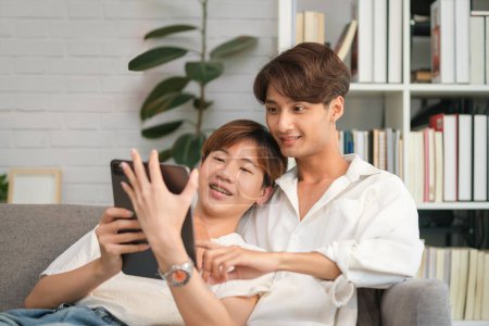 Téléchargez les photos : Heureux couple masculin passer du temps ensemble regarder la vidéo, achats en ligne sur tablette numérique. LGBT, amour, mode de vie matrimonial. - en image libre de droit