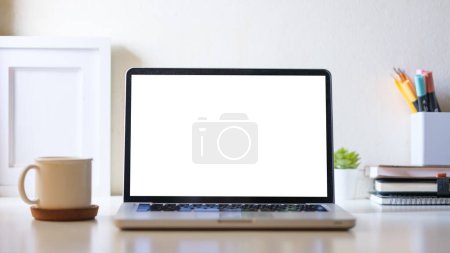 Téléchargez les photos : Vue de face de l'ordinateur portable, tasse de café, cadre photo et papeterie sur table blanche. - en image libre de droit