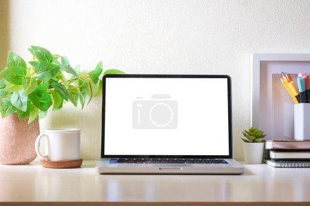 Photo for Simple workplace with laptop, cup of coffee, picture frame and houseplant on white table. - Royalty Free Image