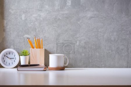 Foto de Lugar de trabajo creativo con taza de café, reloj, maceta y portalápices en la mesa blanca. - Imagen libre de derechos