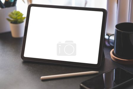 Photo for Closeup shot of digital tablet with white screen, stylus pen, coffee cup and smartphone on black wooden table. - Royalty Free Image