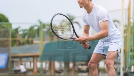 Photo for Young male tennis player holding a racket and standing in a ready position. - Royalty Free Image