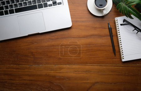 Photo for Top view of laptop computer, coffee cup, notepad and glasses on wooden working desk. Copy space for your text. - Royalty Free Image