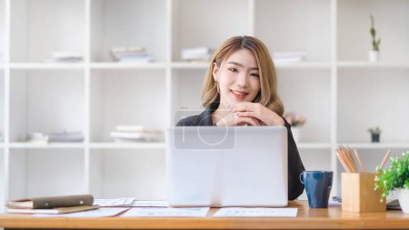 Foto de Retrato de la mujer de negocios sentada en el escritorio con el ordenador portátil y sonriendo a la cámara. - Imagen libre de derechos