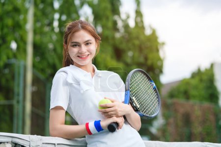 Téléchargez les photos : Belle joueuse de tennis en costume blanc appuyée sur le filet et souriante à la caméra. Sport, compétition et mode de vie actif concept. - en image libre de droit