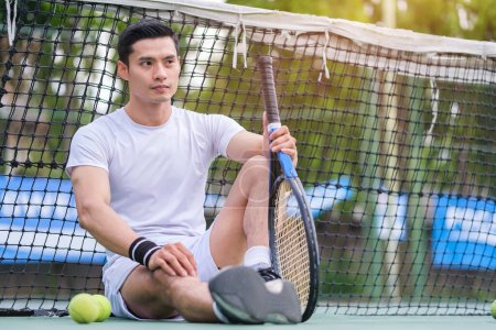Téléchargez les photos : Joueur de tennis masculin épuisé assis sur le terrain contrarié par l'échec ou la perte de la concurrence. - en image libre de droit