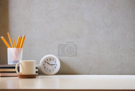 Foto de Minimal workplace with books, alarm clock and flower pot on white table. - Imagen libre de derechos