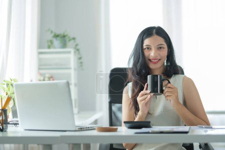 Foto de Atractiva joven empresaria sosteniendo una taza de café y sonriendo a la cámara. - Imagen libre de derechos