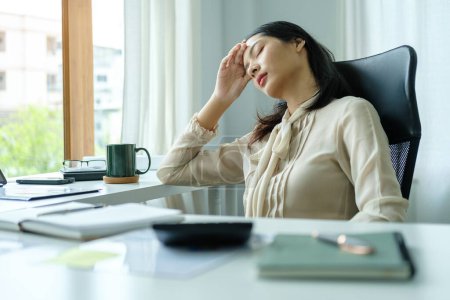 Foto de Mujer empresaria asiática agotada que sufre de dolor de cabeza tocando templos, estrés en el trabajo o migraña. - Imagen libre de derechos