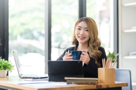 Téléchargez les photos : Millennial businesswoman sitting at her workplace with financial document and smiling to camera. - en image libre de droit