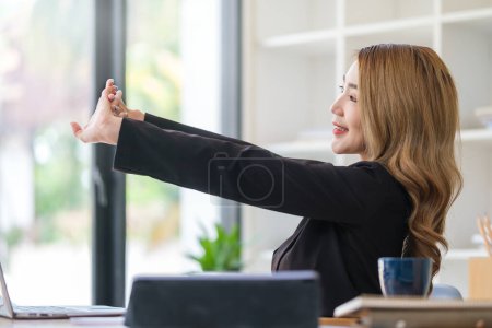 Téléchargez les photos : Jolie jeune femme étirant les bras tout en se relaxant sur son lieu de travail. - en image libre de droit