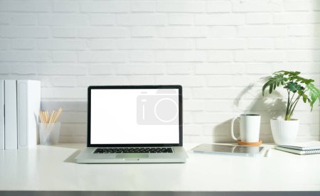 Foto de Ordenador portátil, taza de café y libro en la mesa blanca contra la pared de ladrillo. Pantalla en blanco para su texto publicitario. - Imagen libre de derechos