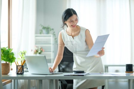 Téléchargez les photos : Belle femme d'affaires asiatique en utilisant un ordinateur portable et en vérifiant le document financier au bureau. - en image libre de droit