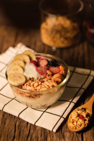 Foto de Cuenco de yogur con bayas granola y plátano sobre mesa de madera. Comida saludable, vegetariana, dieta y concepto de pérdida de peso. - Imagen libre de derechos