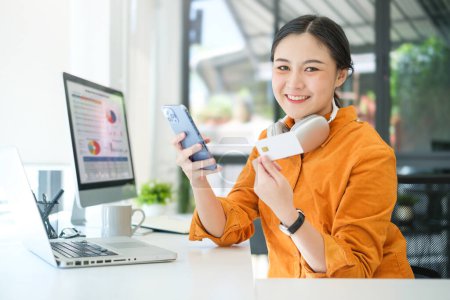 Téléchargez les photos : Souriant jeune femme utilisant un téléphone intelligent et tenant la carte de crédit pour faire du shopping en ligne. - en image libre de droit