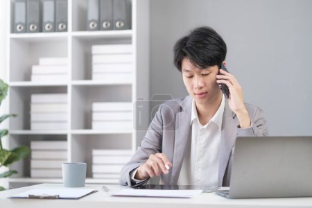Téléchargez les photos : Millennial asiatique homme d'affaires assis dans le bureau moderne et parler sur téléphone mobile. - en image libre de droit