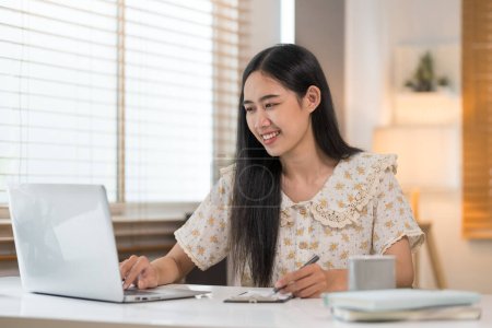 Téléchargez les photos : Belle jeune femme à l'aide d'un ordinateur portable et de prendre des notes sur ordinateur portable. - en image libre de droit