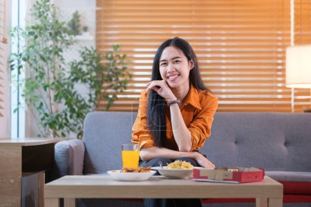 Foto de Mujer asiática bastante joven viendo la televisión y disfrutando de comer pizza. Vida doméstica, comida para llevar y comida rápida. - Imagen libre de derechos