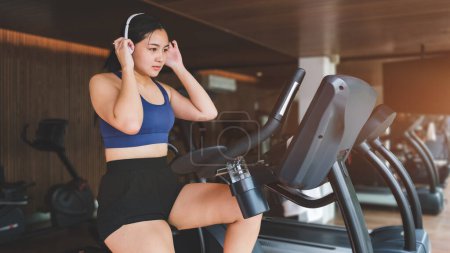 Photo for Beautiful young woman wearing headphone, doing cardio workout, cycling bikes in gym. - Royalty Free Image