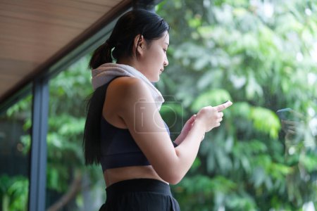 Foto de Mujer joven en ropa deportiva comprobar el teléfono mientras descansa después del entrenamiento en el gimnasio. - Imagen libre de derechos