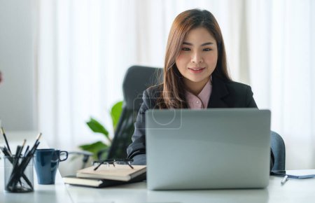 Téléchargez les photos : Jeune asiatique femme de bureau assis dans un bureau lumineux et travaillant sur ordinateur portable. - en image libre de droit