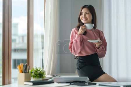 Téléchargez les photos : Asiatique femme de bureau travailleur boire du café et de travailler à lumineux bureau moderne. - en image libre de droit