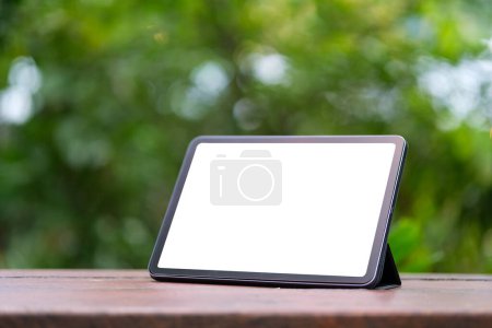 Téléchargez les photos : Tablette numérique avec écran blanc sur table extérieure en bois. Écran vierge pour votre message texte publicitaire. - en image libre de droit
