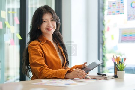 Foto de Sonriendo asiático mujer gráfico diseñador usando sentado frente de la computadora sat su oficina. - Imagen libre de derechos